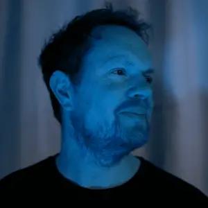 Headshot photograph of The Velvet Shadow with a blue filter.