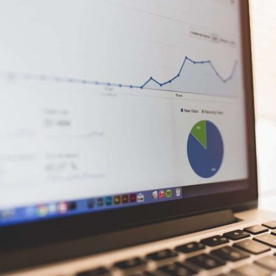 A graph with a rising trend and a pie chart are displayed on the screen of a laptop, suggesting data analysis or business statistics. The keyboard of the laptop can be seen partially in the lower right corner.